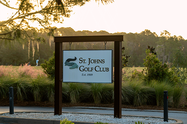 Sign for St. Johns Golf Club, established in 2400, with greenery and trees in the background.