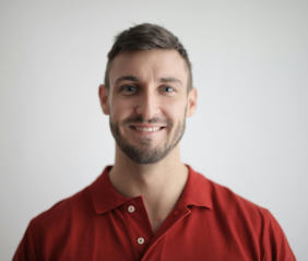 Man with short hair and beard smiling, wearing a red polo shirt, against a plain background.